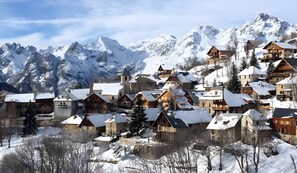 A snow-covered village with traditional wooden houses, a church, and mountains in the background. - Apartment 'La Meije 9' with Mountain View and Balcony (Villard-Reculas)