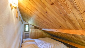 Un dormitorio en el ático con vigas de madera, una cama, una ventana y una puerta.