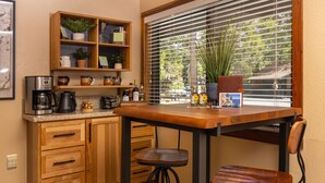 A kitchen with wooden cabinets, a coffee maker, a table, and a window with blinds.