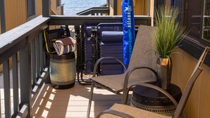 A balcony with a view of the ocean, a chair, a small table, and a potted plant.