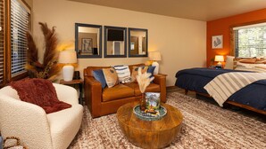A cozy living room with a sofa, a round coffee table, and a bed.