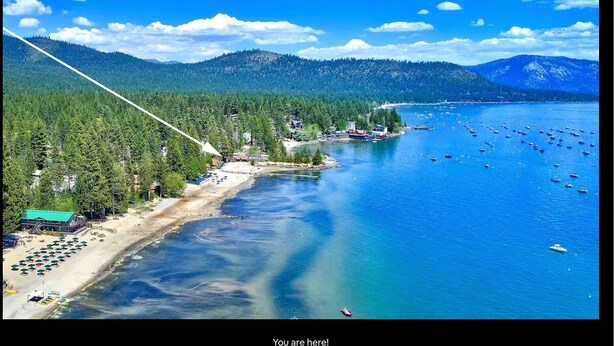 A coastal area with a beach, boats, and forested hills.