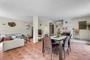 Una sala de estar con sofá, una mesa de comedor con sillas, chimenea y una zona de cocina.