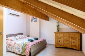 Un dormitorio con techo de madera, una cama con ropa de cama floral, un aparador de madera y un equipo de aire acondicionado.
