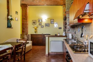 A kitchen with a brick wall, wooden cabinets, a dining area with a table and chairs, and a small refrigerator.