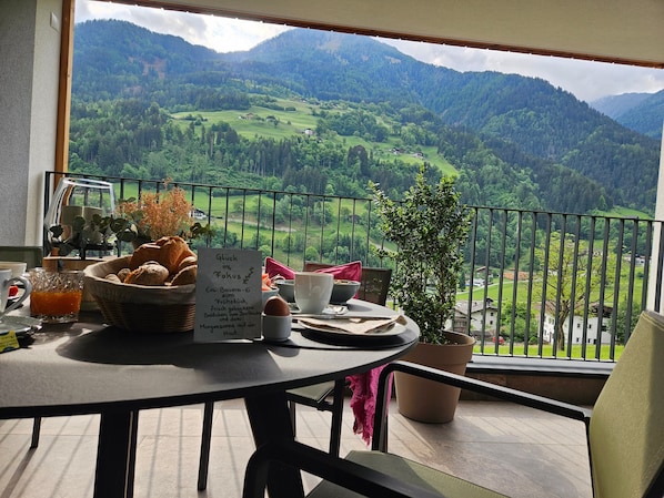A balcony with a table set for breakfast, a menu, and a scenic mountain view.