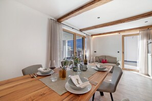 Un coin repas avec une table en bois dressée pour deux personnes, un canapé et une vue sur l’extérieur.