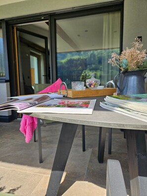 Une table avec des magazines, une serviette rose, un pichet en métal et un vase rempli de fleurs.