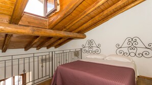 Un dormitorio con techo de madera, cama con colcha rosa y cabecera de metal.
