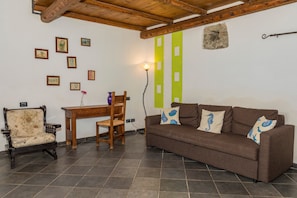 Una sala de estar con un sofá marrón, una silla de madera, una mesa de madera y una pared adornada con cuadros.