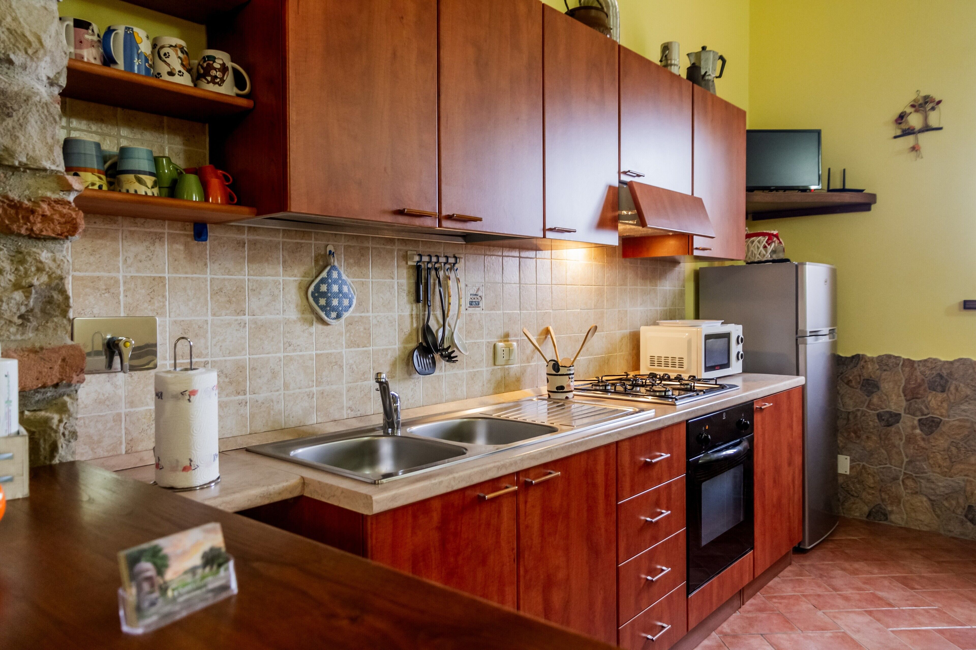 A kitchen with wooden cabinets, a stainless steel sink, a microwave, a refrigerator, and a gas stove.