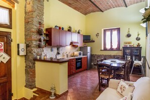 Une cuisine avec un mur en pierre, des placards en bois, un four à micro-ondes et un coin repas comprenant une table et des chaises.