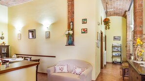 Ein Wohnzimmer mit einer Couch, einem Essbereich mit Tisch und Stühlen, einer Küchenzeile mit Arbeitsplatte und Regalen sowie einem Kamin aus Backsteinen.