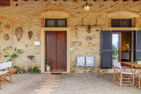 A stone building with a wooden door, a small table with chairs, and potted plants.
