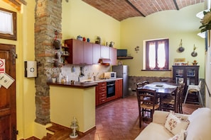 A kitchen with a stone wall, wooden cabinets, a microwave, and a dining area with a table and chairs.