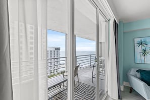 A balcony with a view of the ocean and buildings, a chair, a table, and a painting on the wall. - North Hampton 1606 (Myrtle Beach)