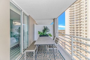A balcony with a patterned floor, a potted plant, and a view of a high-rise building. - North Hampton 1607 (Myrtle Beach)