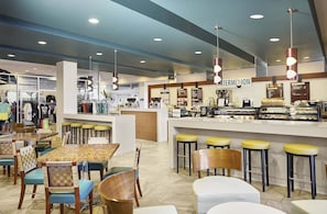 A modern cafe with a central counter, bar stools, and a seating area with tables and chairs.