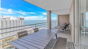 Un balcone con vista sull'oceano e sugli edifici, un tavolo, sedie e una porta in vetro.