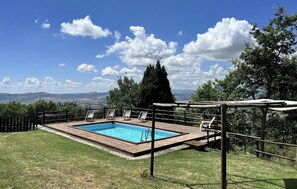A rectangular swimming pool with a wooden deck, surrounded by a wooden fence and lounge chairs.