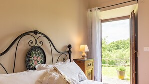 A bed with a floral headboard, a bedside lamp, and a view of a balcony with greenery.