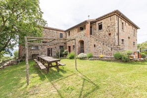 Un bâtiment en pierre avec une pergola en bois et une table de pique-nique dans la cour.