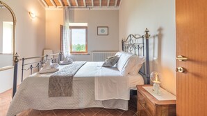 A bedroom with a bed, bedside table, lamp, and a view of the outdoors.