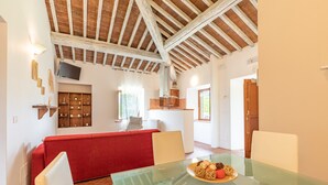 A dining area with a glass table, red sofa, and wooden beams on the ceiling.