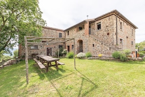 Un bâtiment en pierre avec une pergola en bois et une table de pique-nique dans la cour.