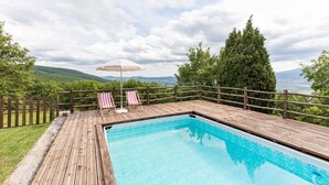 A wooden deck with a swimming pool, two striped lounge chairs, and a beach umbrella.