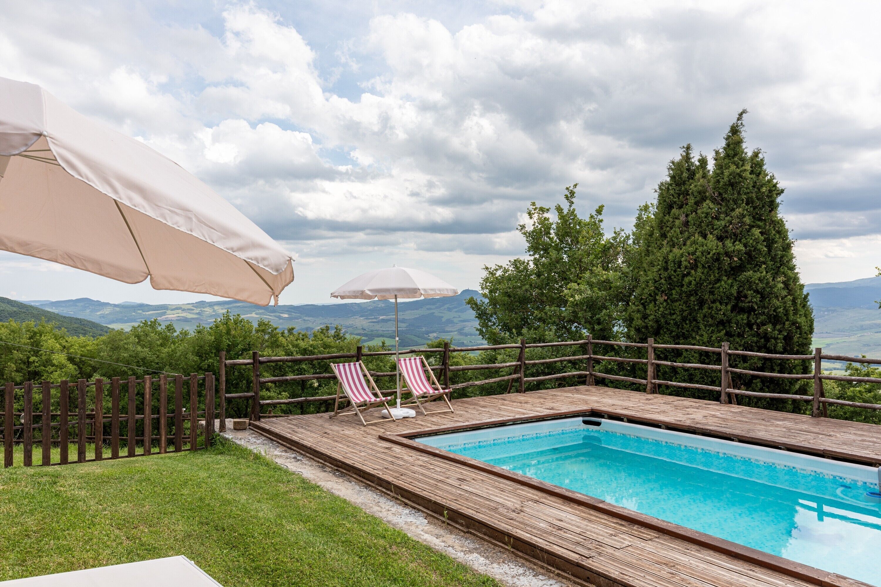 En træterrasse med swimmingpool, to stribede liggestole og et træhegn.