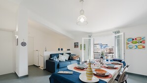 A dining area with a table set for a meal, a sofa in the background, and a kitchen area visible through an open door.