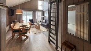 A spacious room with a wooden floor, a dining table with chairs, a sofa, a ladder, and a large window providing a view of the outdoors. - Stunning apartment in Ljørdalen (Ljørdalen)