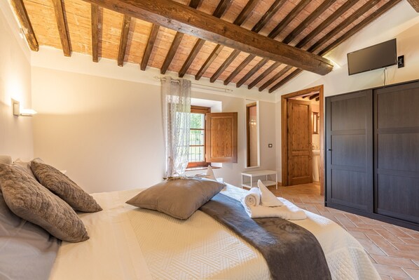 A bedroom with a wooden ceiling, a bed with pillows, a TV mounted on the wall, and a wardrobe.