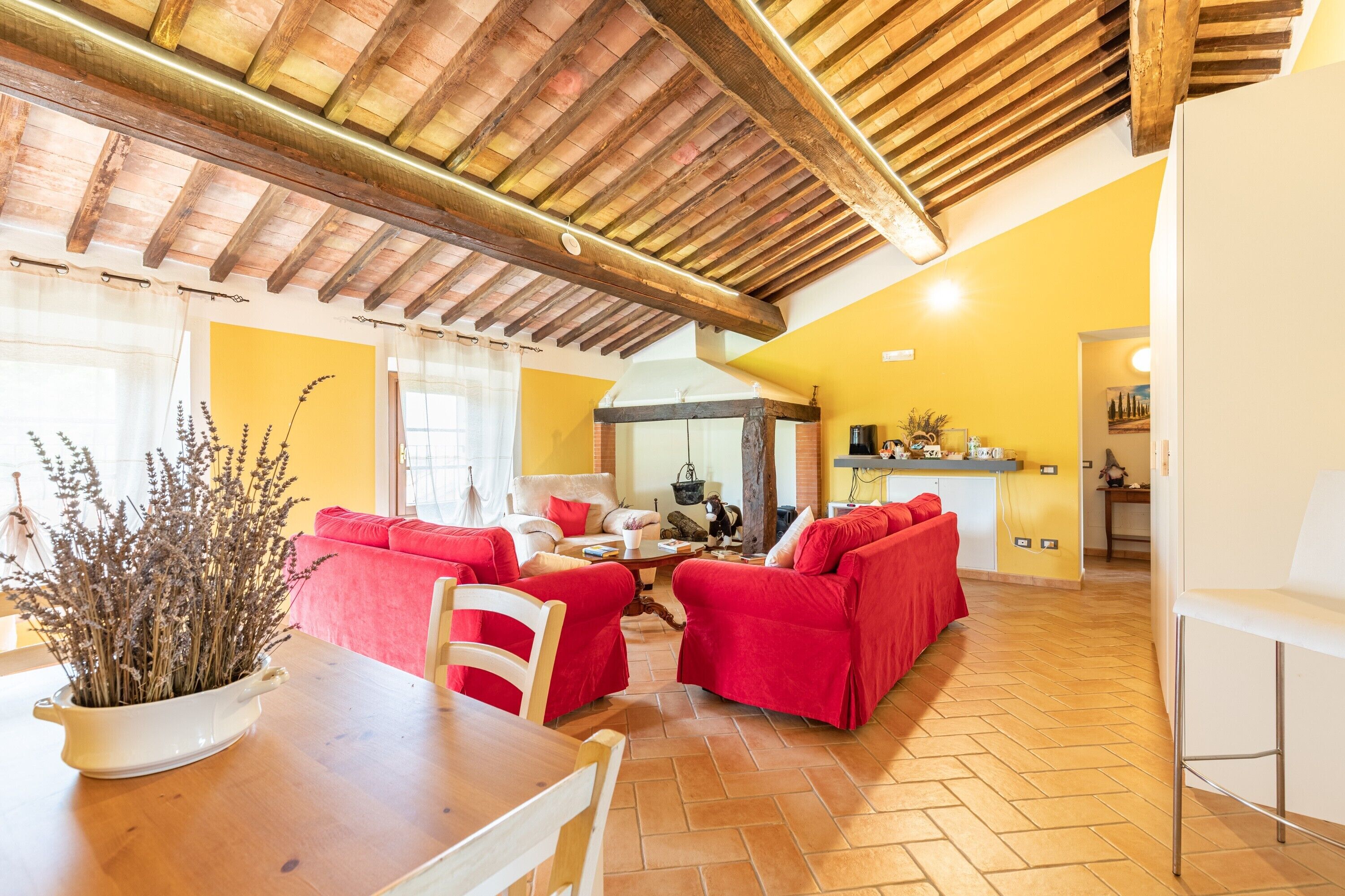 Uma área de refeições com mesa e cadeiras de madeira, sofá vermelho e um vaso com planta.