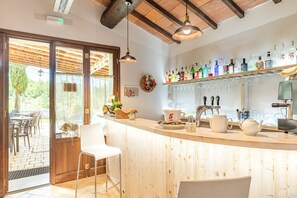 A kitchen with a wooden bar, a coffee machine, and a variety of bottles on the shelf.