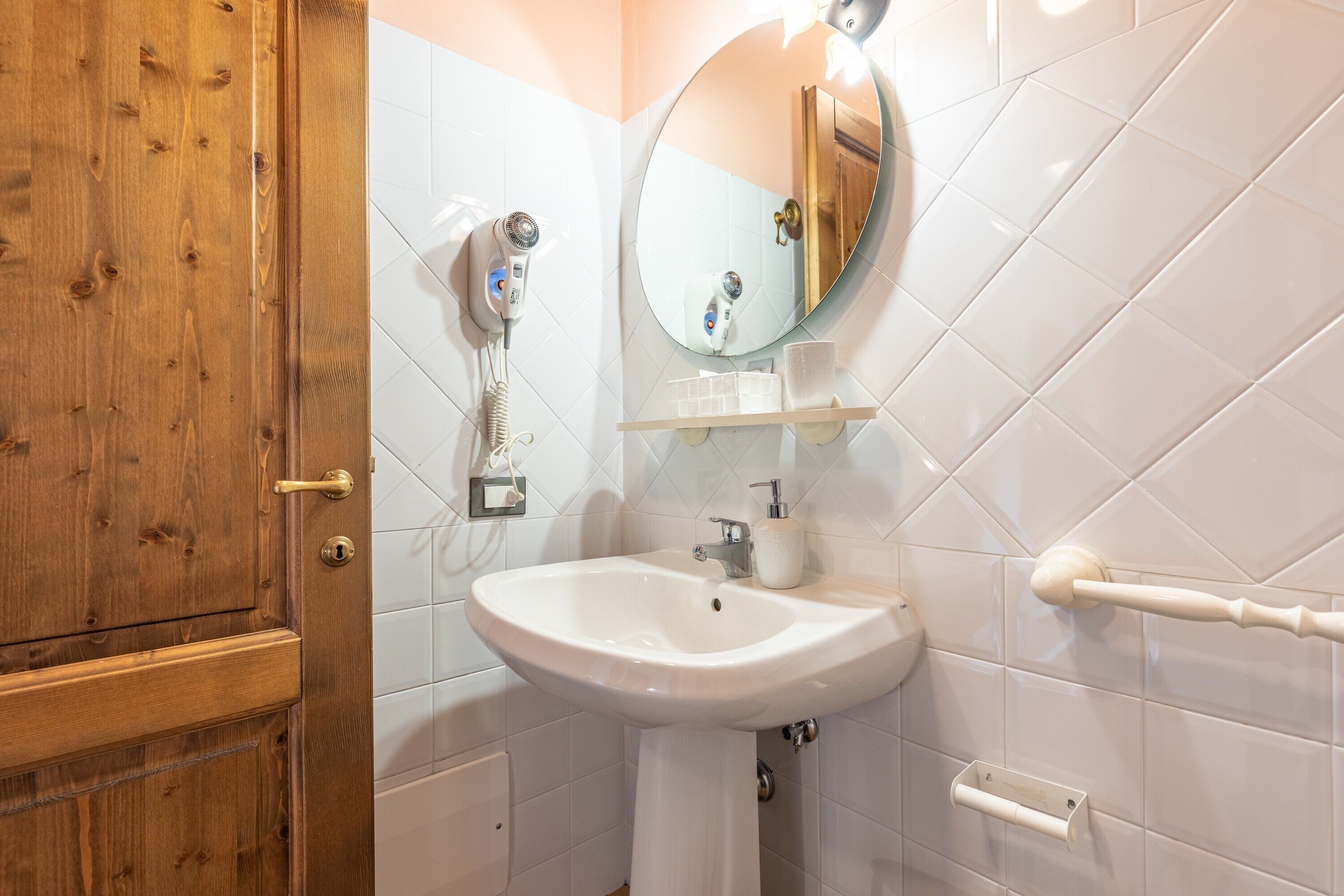Une salle de bain avec une porte en bois, des carreaux blancs, un lavabo blanc, un miroir et un porte-serviettes.