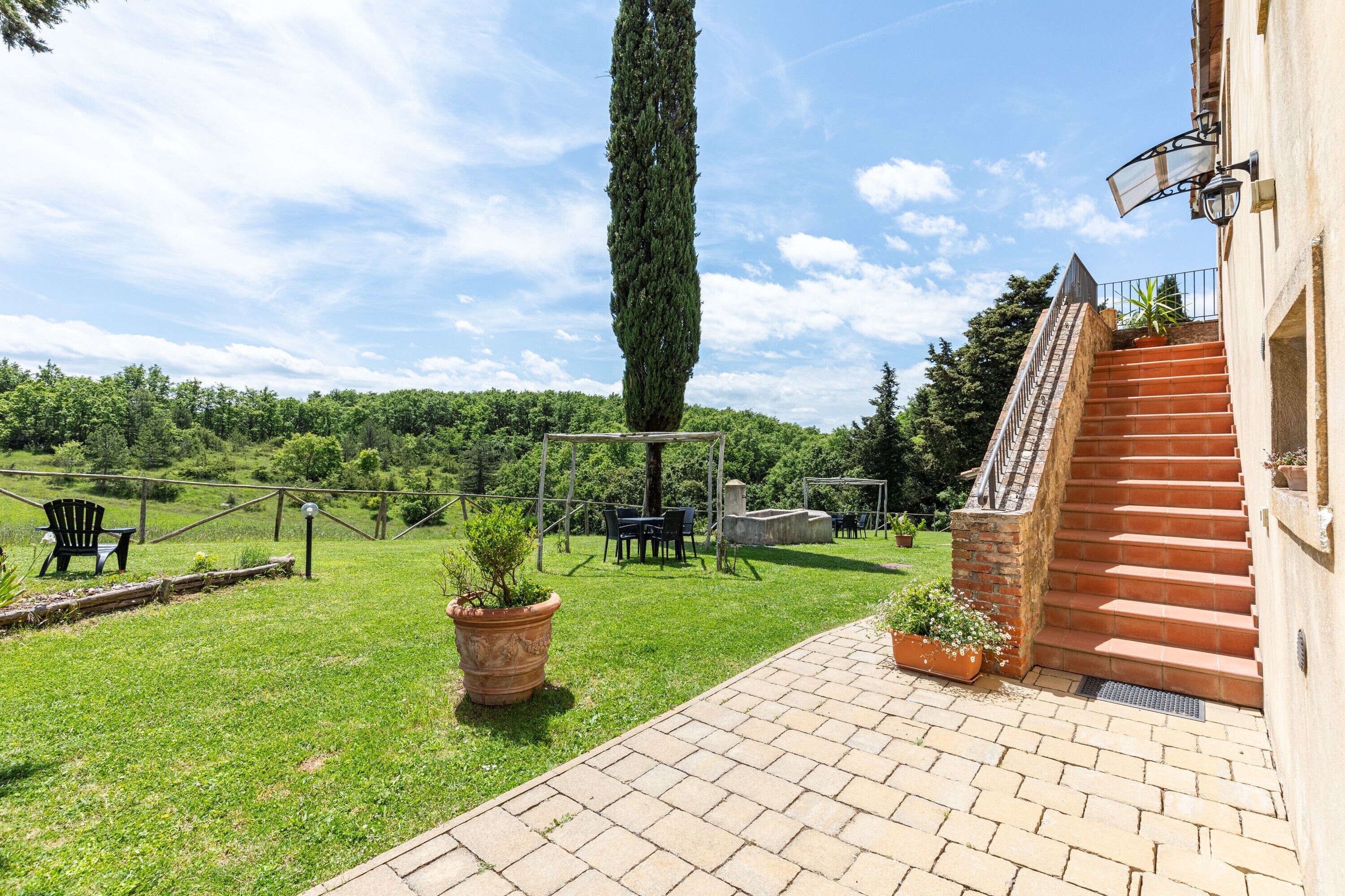 Eine Terrasse mit Backsteinpflaster, ein hoher Baum und eine Treppe, die zu einem Gebäude führt.