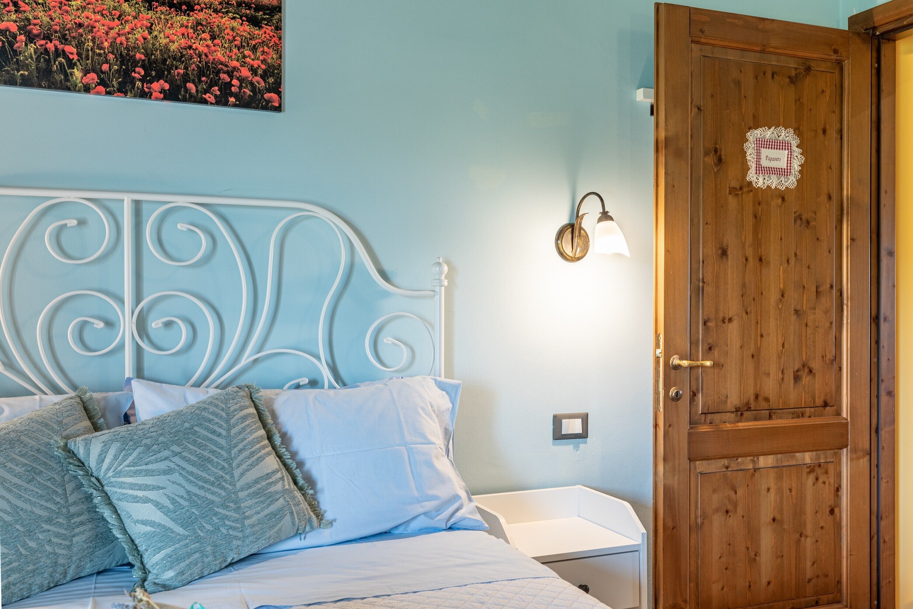 Une chambre à coucher avec un cadre de lit en métal, du linge de lit blanc, une porte en bois et un luminaire fixé au mur.