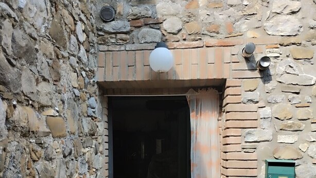 Entrada de un edificio de piedra con una puerta, un accesorio de iluminación, un buzón verde y un timbre de metal.