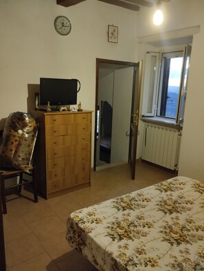 A bedroom with a bed, a dresser, a television, a clock, a window, and a door leading to another room. - Apartment 'Casa Palmira' (Parrano)