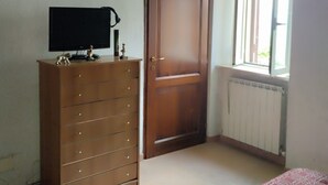 Un dormitorio con un aparador de madera, una puerta, un ventanal y un radiador.