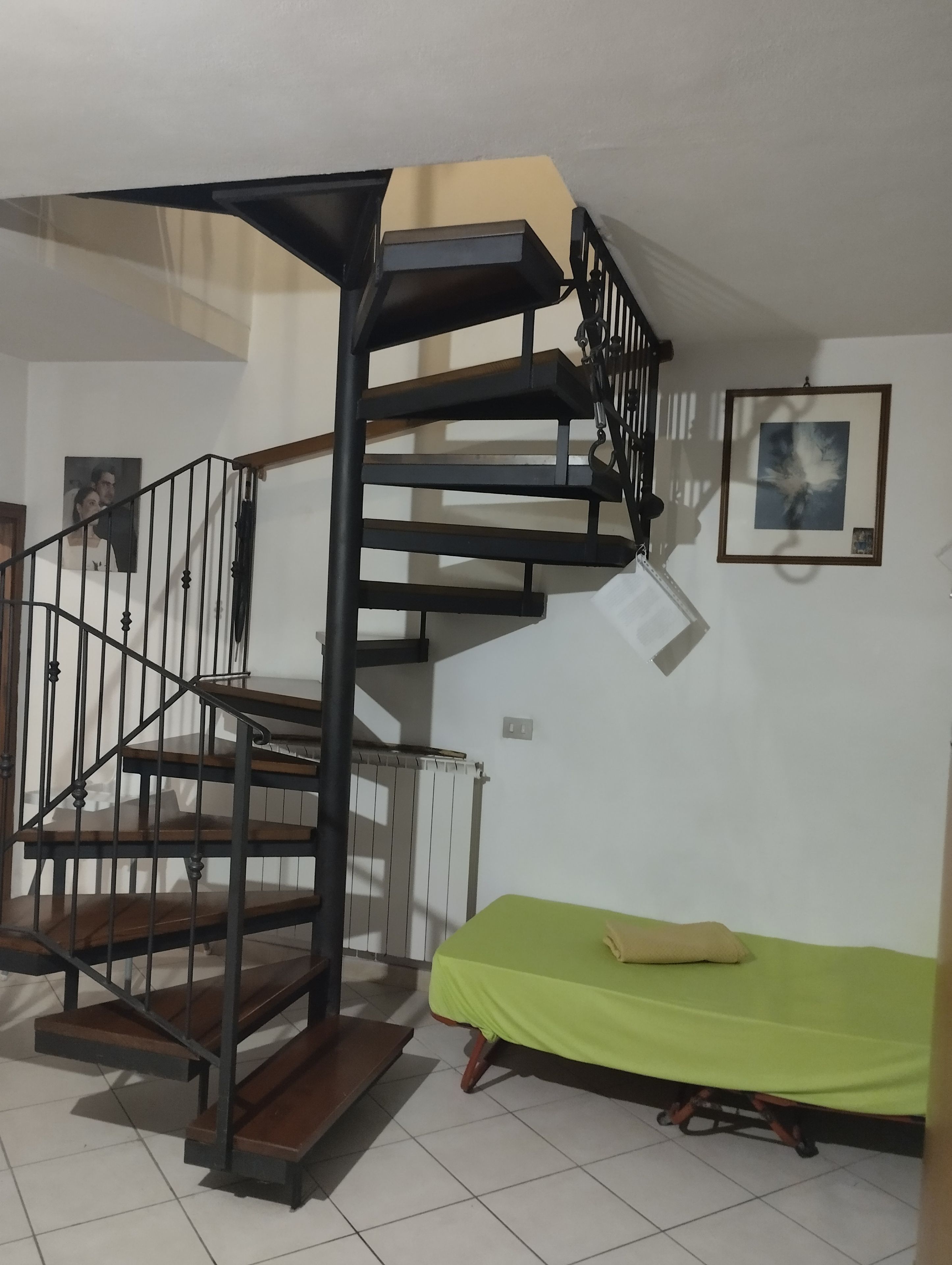 A spiral staircase with a green bed and a framed picture on the wall.
