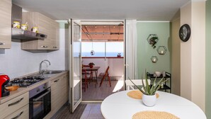 A modern kitchen with a stove, sink, and cabinets, leading to a dining area with a table and chairs. - Apartment 'Etna Home' with Sea View, Wi-Fi and Air Conditioning (Santa Venerina)