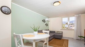 A dining area with a white table and chairs, a potted plant, and a gray sofa with a view through a window. - Apartment 'Etna Home' with Sea View, Wi-Fi and Air Conditioning (Santa Venerina)