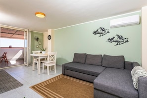 A living room with a sofa, a dining table with chairs, a small rug, and wall decorations.