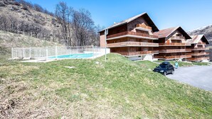 A multi-story building with balconies, a swimming pool, and a parking area. - Apartment 'Les Arolles' with Mountain View, Shared Pool and Balcony (Valloire)