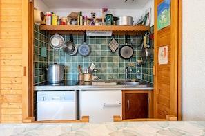 Una cucina compatta con un mobiletto in legno, una lavastoviglie e diversi utensili e pentole da cucina.