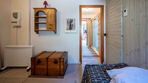 A bedroom with a wooden chest, a radiator, a wooden cabinet, a framed picture, and a bed with patterned bedding. - Apartment 'Les Arolles' with Mountain View, Shared Pool and Balcony (Valloire)