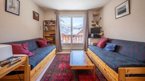 A cozy room with two wooden sofas, a small table, a bookshelf, and a view of snowy mountains through a glass door. - Apartment 'Les Arolles' with Mountain View, Shared Pool and Balcony (Valloire)